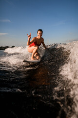 smiling woman rides on surfboard and shows hand gesture