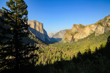 View of a canyon, forest lit by the sun ,mountains and waterfall against a blue sky in Yosemite Valley, California, USA