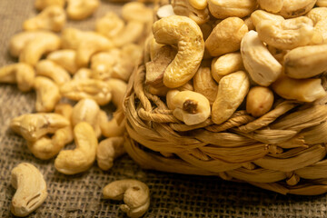Cashew nuts in a wicker basket and cashew nuts scattered on burlap with a rough texture surface texture. Close up.