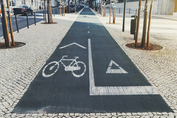 Wide-angle view of an asphalt bicycle lane and a running track surfaces in urban settings surrounded by paving-stone, small trees, and a small road with cars, sunny day, Lisbon, Portugal