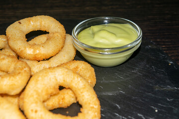 Onion rings and a glass saucepan with sauce. Close up.
