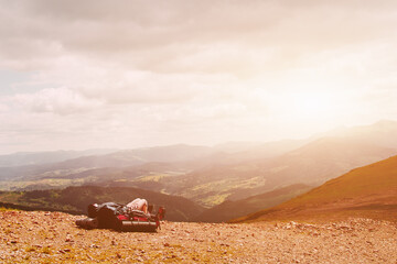 Young blonde woman tourist resting on a hiking backpack in the mountains