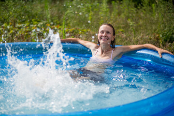 Beautiful woman splashing in inflatable swimming pool outdoor, having fun