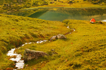 Orange tent near the lake in the mountains