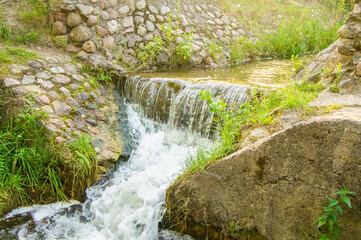 Beautiful sunny waterfall of a mountain river. Old stone bridge with seething water