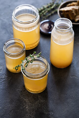 Glass jar with yellow fresh bone broth on dark gray background top view. Healthy low-calories food...