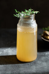 Fresh vegetable bone broth in glass jar with herb on dark gray background. Healthy dieting food are rich in vitamins, collagen and anti-inflammatory amino acids