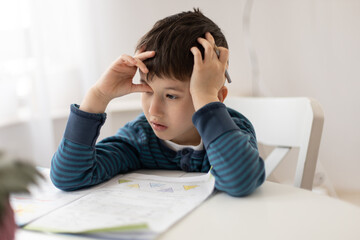Portrait of young boy struggling with his homework at home. Children home education concept....