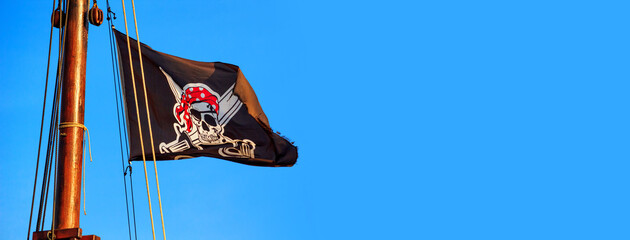 The pirate flag or the Jolly Roger - old shabby black flag with a skull waving on the mast of a sailing ship