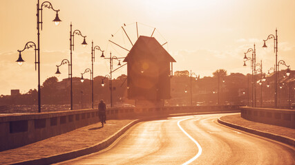 Morning city landscape - view of the road with the cyclist and the wooden windmill before the entrance to the Old Town of Nessebar, on the Black Sea coast of Bulgaria