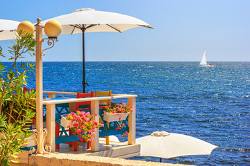 Seaside landscape - view of the cafe on the embankment against the background of the sea with sailboat, in the Nesebar, on the Black Sea coast of Bulgaria