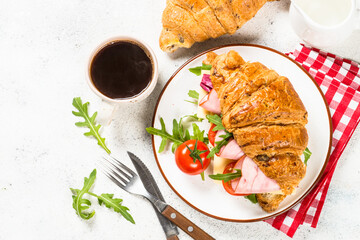 Croissant sandwich with coffee on white table.