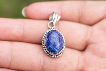 Outdoor close up of hand showing lapis lazuli mineral gemstone oval pendant