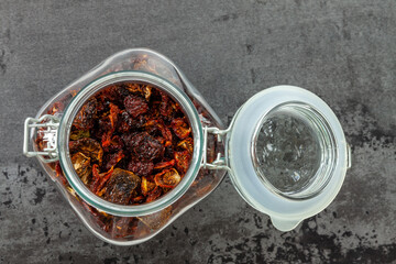 Open glass jar with dry tomatoes top view. Storage of dried dehydrated vegetables. Gray background, flat lay.