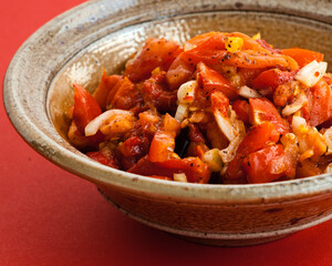 Homemade one-pot cooked salad meal made of baked peppers, tomato and preserved lemons. Served in handmade ceramic bowl. Close-up view, red background.