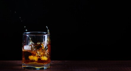 Ice cubes falling into a glass of whiskey with flying splashes on a black background
