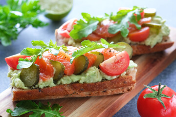 Sandwiches with salmon, avocado, pickled cucumbers, cherry tomatoes and arugula on wooden cutting board