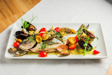 Grilled dorado fish on a white plate with cherry tomatos and mussels