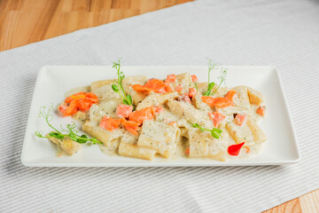 Paccheri pasta with cream sauce and salmon on a white plate