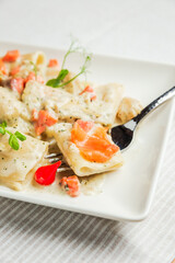 A close-up of paccheri pasta with cream sauce and salmon on a fork, on a white plate