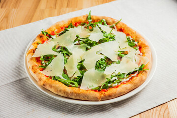 Pizza with arugula or rocket and parmesan cheese on a white plate