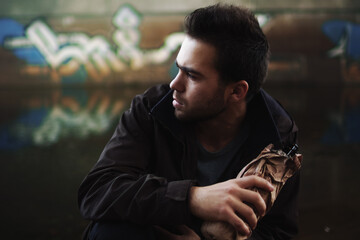 Close-up of a young brunette male alcoholic on the street under the bridge.