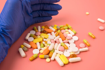 Close up of doctor hand in blue glove and many different pills on pink background.