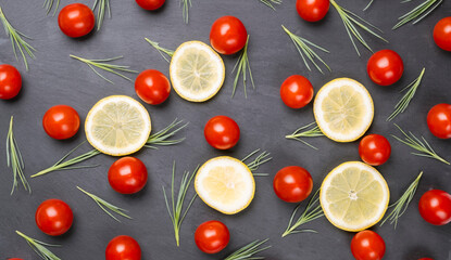 Red cherry tomatoes, orange and lemon slices and green salad leaves on dark black background.