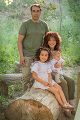 Family consisting of father mother baby and girl sitting on a log of wood in a grove.