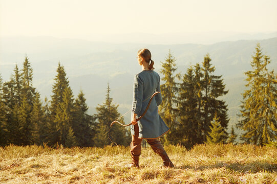 Woman shooting with a bow in the mountains. Young Caucasian female archer shooting with a bow at sunset. Scanned film.