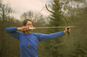Young caucasian woman archer shooting in the forest with a bow. Scanned film