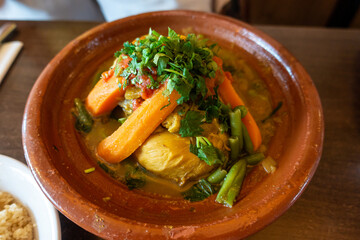 Chicken tagine,  Moroccan dish, with vegetables served on a rustic pottery place.