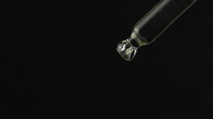 Oil or liquid dropper or pipette in extreme macro close up. Drop of yellow cosmetic lavender oil falling on black background. Eyedropper squeezing out meds droplets.