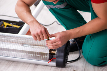 Young male contractor repairing heater indoors