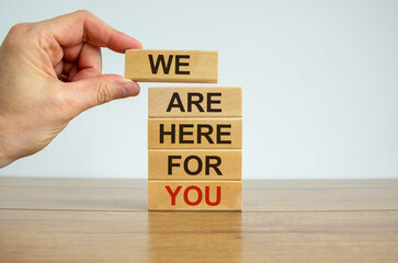 Concept of building success foundation. Men hand put wooden blocks on the stack of wooden blocks. Text 'we are here for you'. Beautiful white background, copy space.