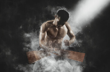 Karate man breaking with hand wooden board on smoke background. Sports banner