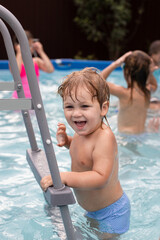a smiling two-year-old boy swims in a pool on the front lawn