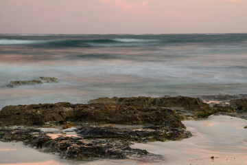 Long exposure shot. Surreal blurred sea waves at nightfall. The shore, ocean and rocks with enchanting sunset colors.