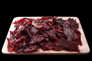 Obraz premium Horse meat jerky, cut into slices, on a wooden board, on a black background