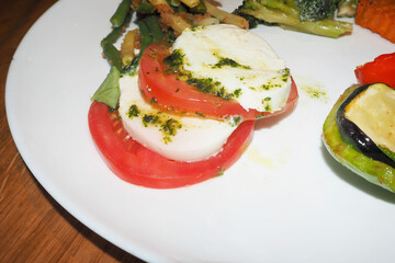 sliced ​​tomato with white soft cheese and garlic dressing on a white round plate with other dishes side view