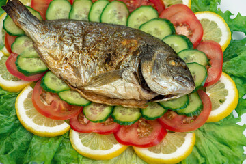 Ggrilled dorado fish with vegetables: salad, tomatoes, cucumber, green pepper and lemon