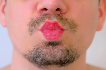 Man with red lipstick on lips giving a kiss on white background, mouth closeup. LGBT, gey, free love concept. Bearded unrecognizable young guy with moustache.