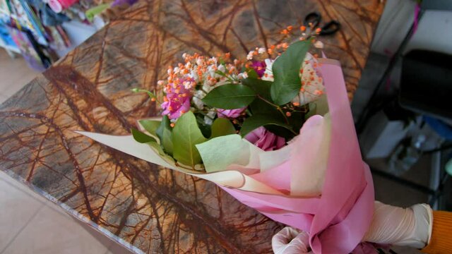 woman wraps fresh flower bouquet with pink foil at table