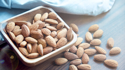 Almonds in small wooden bowl. Almonds laid freely on dark table. Row of bowls with almond nuts, top view. Peeled almond pattern
