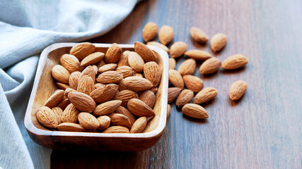 Almonds in small wooden bowl. Almonds laid freely on dark table. Row of bowls with almond nuts, top view. Peeled almond pattern