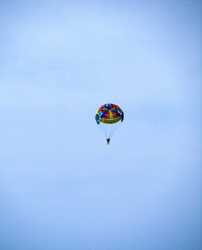 A parachutist with a colored round parachute flies against the blue sky. Vertical photo