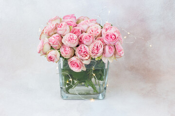 a bouquet of pink roses in a transparent square vase and a garland of lights