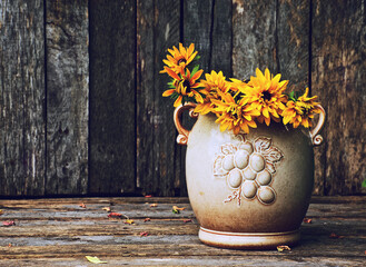 Brown eyed susan or rudbeckia flowers in a vintage pottery vase on wood.