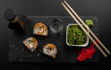 Sushi with eel and wakame hayashi salad lie on a black board made of stone. Top view