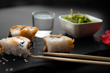 Sushi with eel and hayash wakamei salad lie on a black board made of stone slate